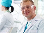 A man in lab coat and goggles smiling for the camera.