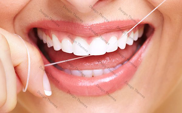 A woman with white teeth holding a tooth pick in her mouth.