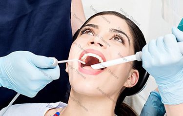 A woman getting her teeth brushed by two dentists.