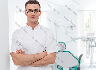A man in glasses and white shirt standing next to a dentist chair.