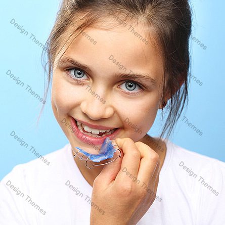 A girl with blue eyes is holding something in her mouth.